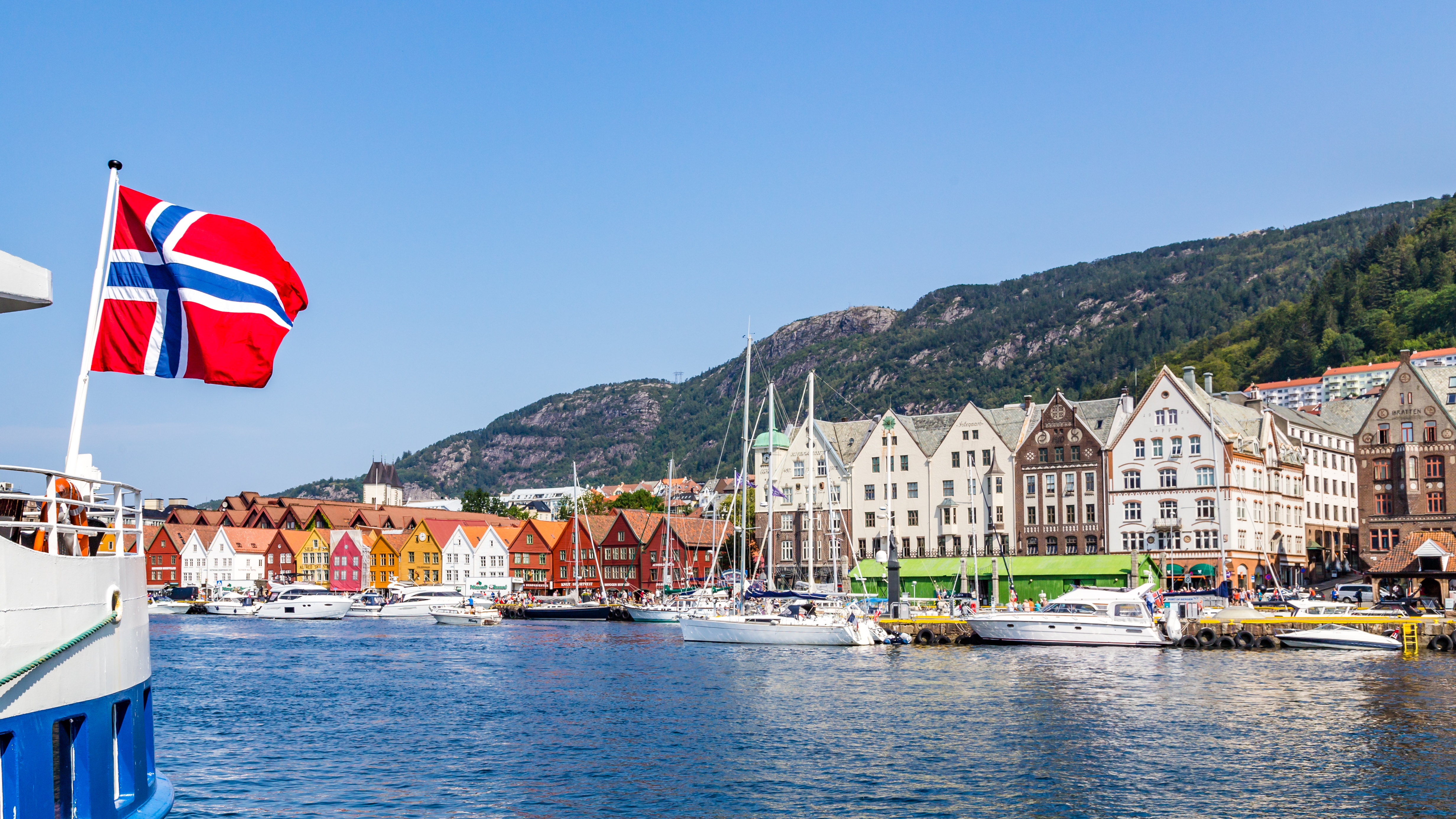 Image of coastal city Bergen, Norway, with the Norwegian flag flying from a boat.